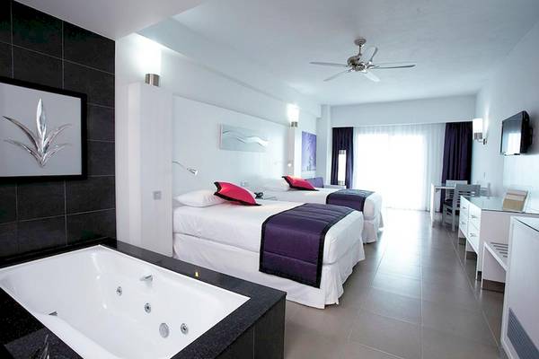 Schlafzimmer im Riu Palace Peninsula Hotel mit Badewanne, zwei Betten und moderner Einrichtung.