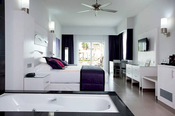 Schlafzimmer im Riu Palace Peninsula mit Bett, Nachttischen, Badewanne und Schreibtisch.
