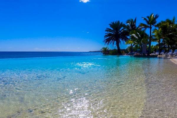 Strand des Anelia Resort & Spa mit kristallklarem Wasser, Sonnenliegen und Palmen
