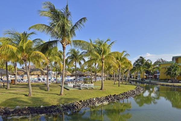 Außenbereich des Melia Las Antillas Hotels mit Palmen, einem Pool und einem Schachspiel auf der Wiese.