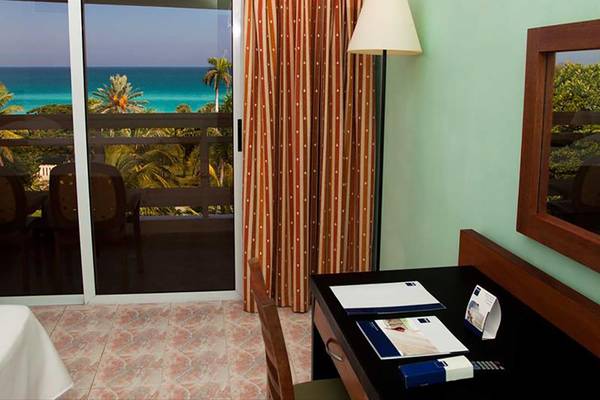 Zimmer im Occidental Arenas Blancas Hotel mit Meerblick, Glastür und Schreibtisch.