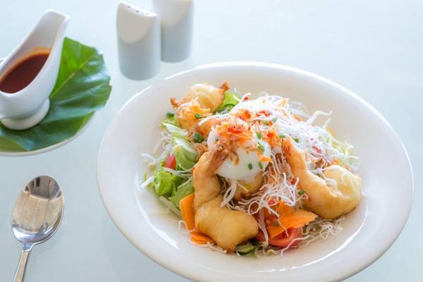 Ein Teller mit einem Salatgericht im Beyond Resort Khao Lak, serviert mit Soße und Besteck.