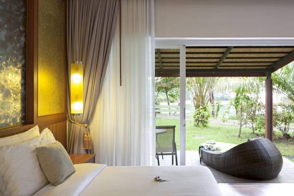 Bett im Zimmer des Beyond Resort Khao Lak mit Blick auf eine Terrasse und Garten.