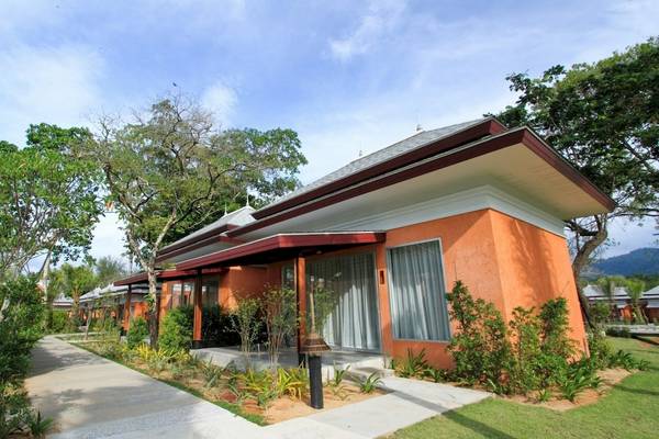 Außenansicht des Beyond Resort Khao Lak mit orangefarbenem Gebäude und grünem Rasen.