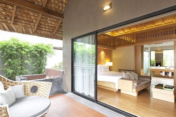 Innenansicht eines Zimmers im Beyond Resort Khao Lak mit großem Bett, Couch und Glaswänden, die zur Außenseite führen.