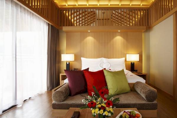 Schlafzimmer im Beyond Resort Khao Lak mit einem Bett, Kissen, Lampen und einem Blumenstrauß.