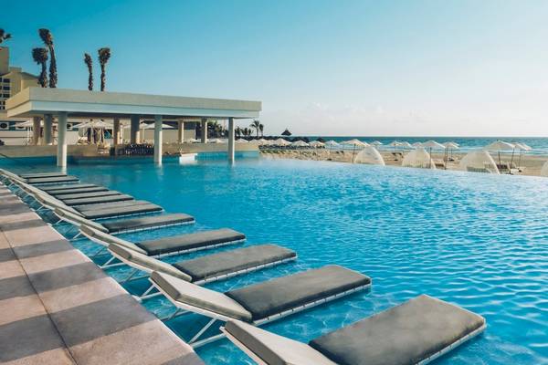 Infinity-Pool am Coral Level at Iberostar Selection Cancun mit Sonnenliegen und Blick auf den Strand.