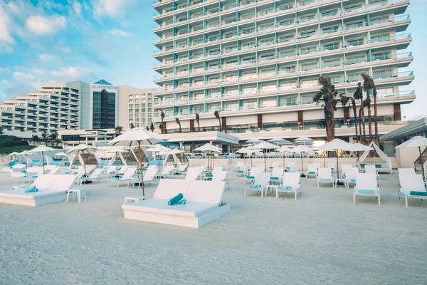 Strand mit weißen Sonnenliegen und Sonnenschirmen vor dem Coral Level at Iberostar Selection Cancun Hotel