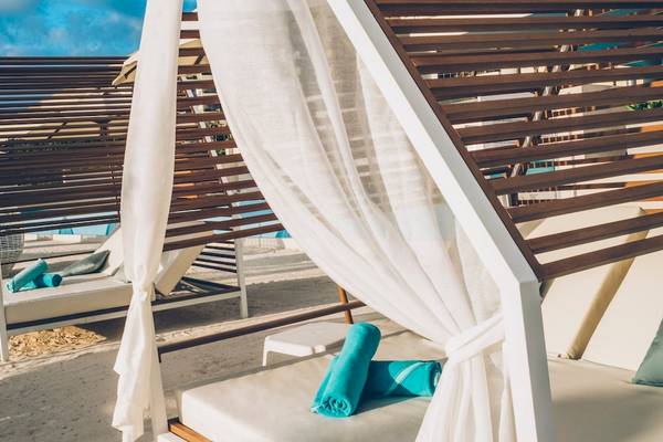 Reihe von Loungebetten am Strand des Coral Level at Iberostar Selection Cancun, bedeckt mit weißen Vorhängen und blauen Handtüchern.