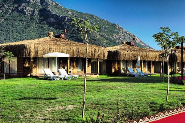 Außenbereich des Sahra Su Holiday Village & Spa mit charakteristischen Strohhut-Hütten und grüner Rasenfläche.