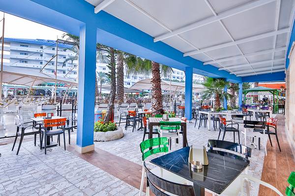 Terrasse des Crystal Admiral Resort Suites & Spa mit Tischen und Stühlen unter Palmen