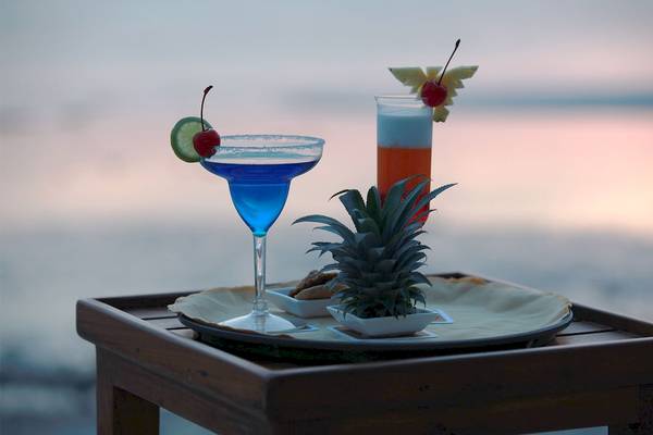 Zwei Cocktails auf einem Holztisch am Strand mit einem Ausblick auf den Horizont.