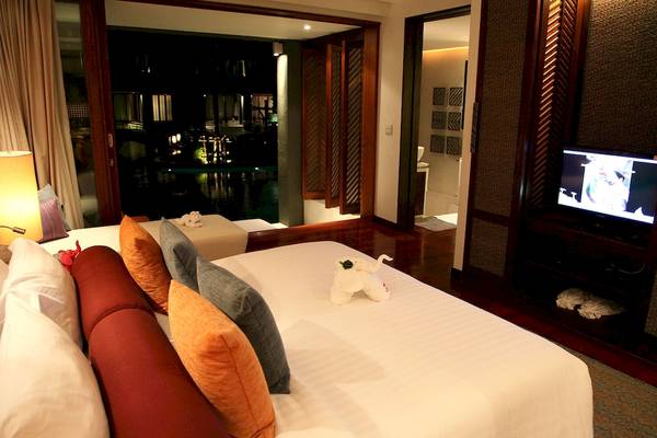 Schlafzimmer im Mai Samui Beach Resort & Spa mit Fernseher, Nachttisch und Bett mit Kissen.