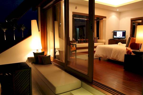 Nachtansicht des Schlafzimmers im Mai Samui Beach Resort mit Panoramafenstern und Blick auf Palmen.