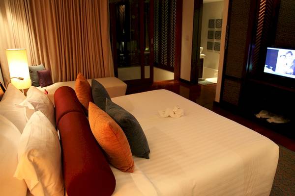 Schlafzimmer im Mai Samui Beach Resort & Spa mit Fernseher, Bett und Kissen.