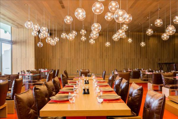 Innenansicht des Restaurants im Maxx Royal Belek Golf Resort mit langen Tischen, Lederstühlen und runden Lampen an der Decke.