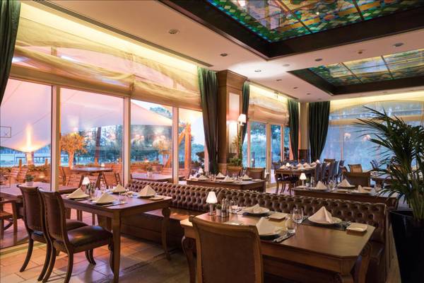 Innenansicht des Restaurants im Maxx Royal Belek Golf Resort mit gedeckten Tischen und buntem Glasdach.