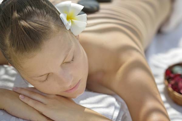 Frau mit Blume im Haar und geschlossenen Augen entspannt sich am Strand im Villa Nautica Paradise Island Resort