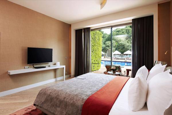Innenansicht eines Zimmers im Maxx Royal Belek Golf Resort mit Fernseher, Bett und Poolblick.