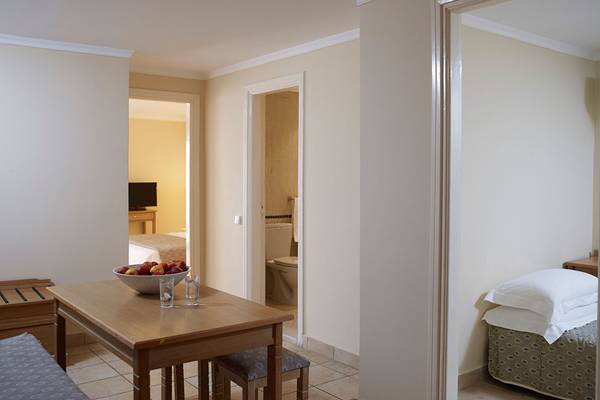 Innenansicht eines Zimmers im Mitsis Family Village Beach Hotel mit Tisch, Obstschale und Schlafzimmer.