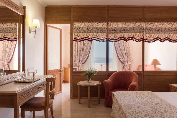 Schlafzimmer im Mitsis Family Village Beach Hotel mit Fenstern, Vorhängen und einem Ausblick auf das Meer.