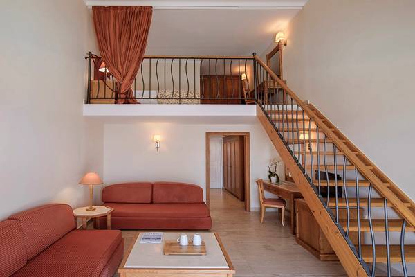 Innenansicht der Suite im Mitsis Family Village Beach Hotel mit Wohnzimmer, Schlafbereich und Treppe.