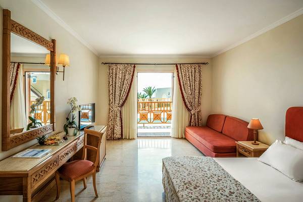 Hotelzimmer im Mitsis Family Village Beach Hotel mit Bett, Sofa, Schreibtisch und Spiegel.