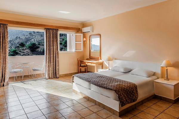 Innenansicht eines Zimmers im Mitsis Family Village Beach Hotel mit Bett, Schreibtisch und Balkon