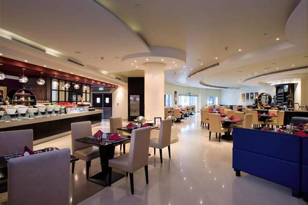 Innenansicht des Restaurants im Al Hamra Residence Hotel mit gepolsterten Stühlen und Tischen.