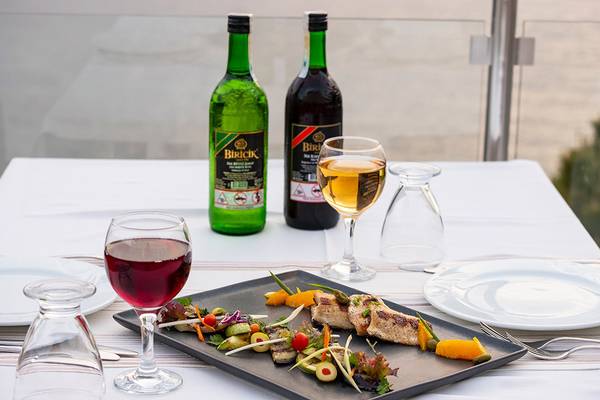 Ein Tisch im Ladonia Hotel mit einem Gericht, zwei Flaschen Biricki Getraenke und Weinglaesern.