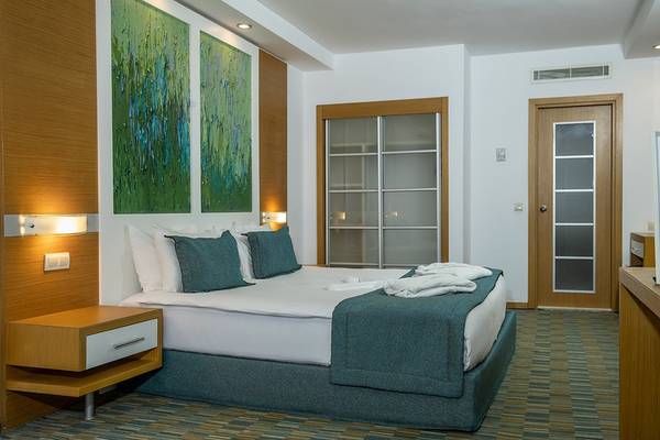 Innenansicht eines Schlafzimmers der Ladonia Hotels Adakule mit einem Bett, Nachttischen und Gemälden.
