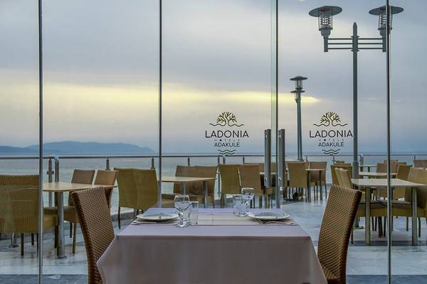Außenbereich des Ladonia Hotels Adakule mit Blick auf das Meer und eine Terrasse mit Tisch und Stühlen.