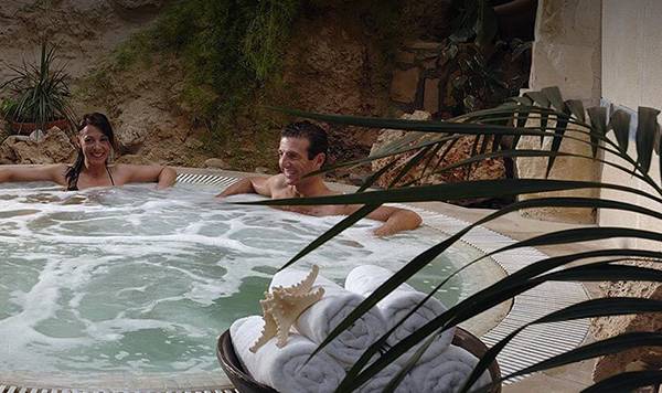 Ein Whirlpool im Freien mit zwei Personen im Coral Beach Hotel & Resorts, umgeben von Pflanzen und einem Tisch.