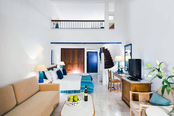 Innenansicht eines Hotelzimmers im Coral Beach Hotel & Resorts mit Bett, Sofa, Schreibtisch und Fernseher.