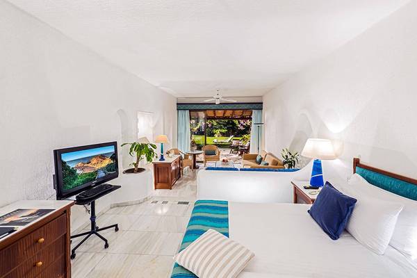 Innenansicht eines Zimmers im Coral Beach Hotel & Resorts mit Bett, Fernseher, Schreibtisch und offener Terrasse.