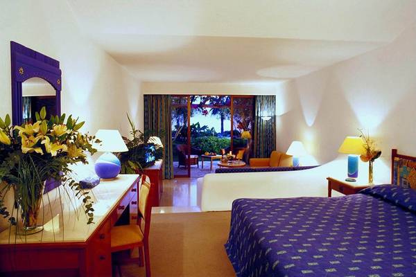 Innenansicht eines eleganten Zimmers im Coral Beach Hotel & Resorts mit Bett, Schreibtisch und Balkon