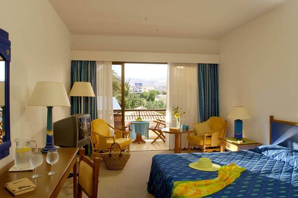 Zimmer im Coral Beach Hotel & Resorts mit Balkon, Fernseher und gemütlichen Möbeln.