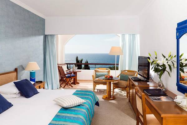 Zimmer im Coral Beach Hotel mit Meerblick, Bett, Balkon, Fernseher und Tisch mit Obst.