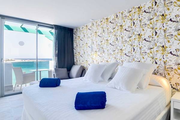 Hotelzimmer im Barceló Teguise Beach Adults Only mit Blick auf das Meer und blauen Handtüchern auf dem Bett.