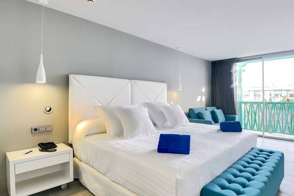 Modernes Hotelzimmer im Barceló Teguise Beach Adults Only mit weißem Bett, blauen Kissen und grünem Balkon.