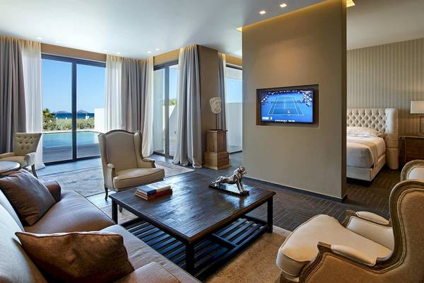 Wohnzimmer im Pelagos Suites Hotel mit Meerblick, inklusive Sofa, Tisch und Fernseher.