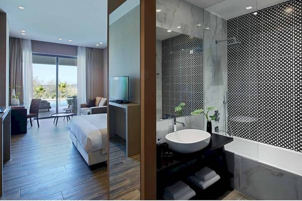Innenansicht eines Zimmers im Pelagos Suites Hotel & Spa mit Bett, Fernseher, Badezimmer und Aussicht.