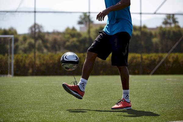 Fußballspieler kickt Ball auf Kunstrasenplatz unter freiem Himmel.