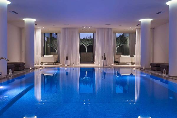Schwimmbecken im Pelagos Suites Hotel und Spa mit weißen Vorhängen und blauer Beleuchtung.