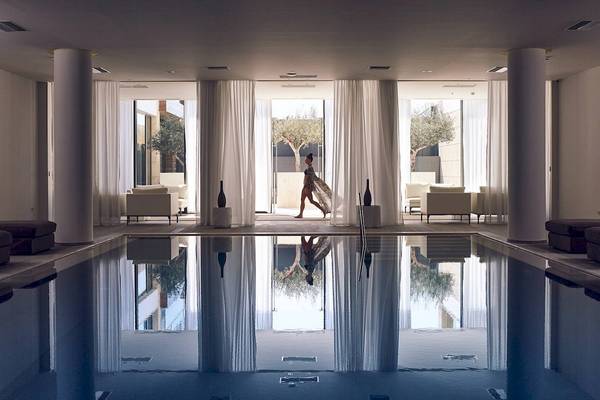 Innenansicht des Schwimmbeckens im Pelagos Suites Hotel & Spa mit einer Person, die durch eine Glastür geht.