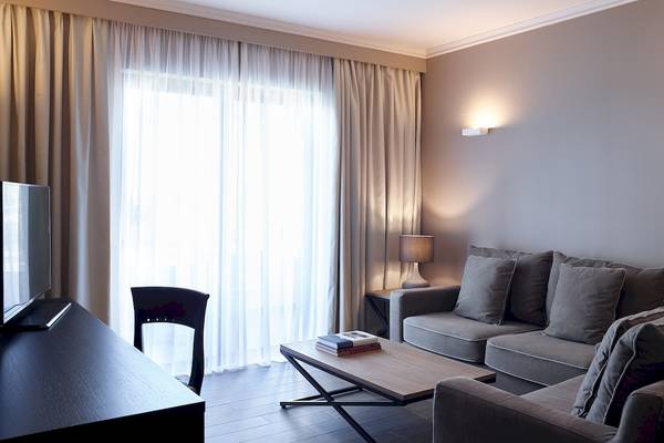 Wohnzimmer im Pelagos Suites Hotel & Spa mit Couch, Tisch, Lampe und Fernseher.