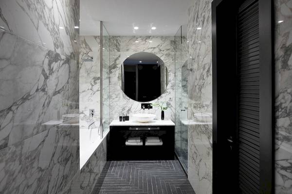 Ein Badezimmer mit Marmorwänden, einem großen runden Spiegel und einer Badewanne im Pelagos Suites Hotel & Spa.