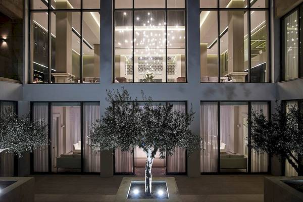 Außenansicht des Pelagos Suites Hotel & Spa mit großen Fenstern und beleuchteten Olivenbäumen.