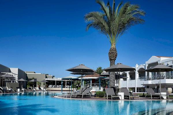 Außenbereich des Pelagos Suites Hotel & Spa mit Swimmingpool, Liegestühlen und Palme