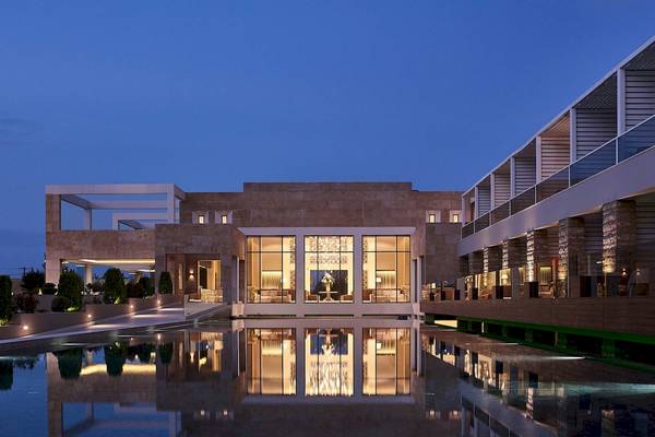 Abendliche Ansicht des Pelagos Suites Hotel & Spa mit beleuchteter Fassade und Wasserreflexion.